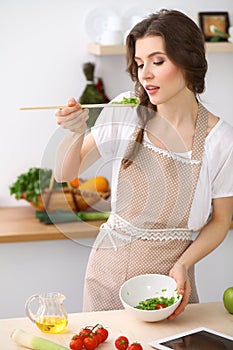 Young brunette woman cooking in kitchen. Housewife holding wooden spoon in her hand. Food and health concept