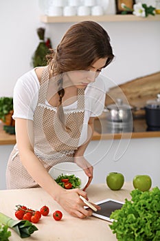 Young brunette woman cooking in kitchen. Housewife holding wooden spoon in her hand. Food and health concept