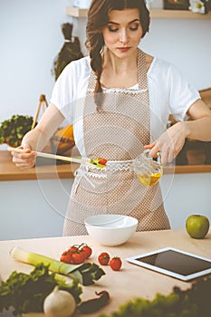 Young brunette woman cooking in kitchen. Housewife holding wooden spoon in her hand. Food and health concept