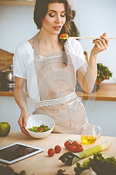 Young brunette woman cooking in kitchen. Housewife holding wooden spoon in her hand. Food and health concept