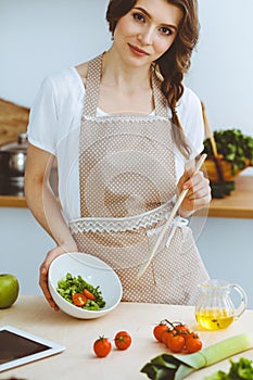 Young brunette woman cooking in kitchen. Housewife holding wooden spoon in her hand. Food and health concept