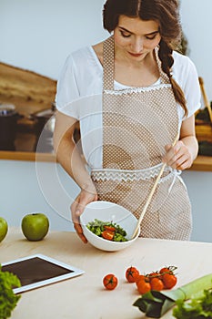 Young brunette woman cooking in kitchen. Housewife holding wooden spoon in her hand. Food and health concept