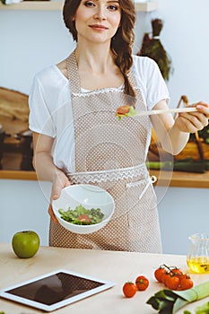 Young brunette woman cooking in kitchen. Housewife holding wooden spoon in her hand. Food and health concept