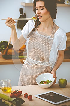 Young brunette woman cooking in kitchen. Housewife holding wooden spoon in her hand. Food and health concept