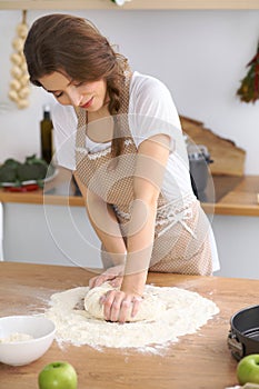 Young brunette woman cooking pizza or handmade pasta in the kitchen. Housewife preparing dough on wooden table