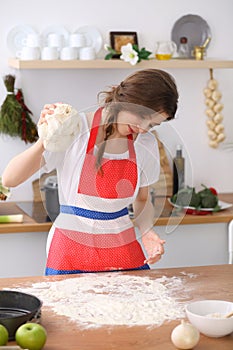 Young brunette woman cooking pizza or handmade pasta in the kitchen. Housewife preparing dough on wooden table. Dieting