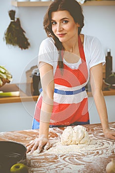 Young brunette woman cooking pizza or handmade pasta in the kitchen. Housewife preparing dough on wooden table. Dieting