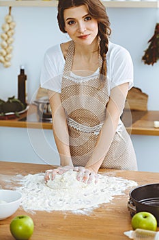 Young brunette woman cooking pizza or handmade pasta in the kitchen. Housewife preparing dough on wooden table. Dieting