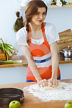 Young brunette woman cooking pizza or handmade pasta in the kitchen. Housewife preparing dough on wooden table. Dieting