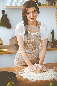 Young brunette woman cooking pizza or handmade pasta in the kitchen. Housewife preparing dough on wooden table. Dieting