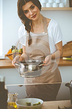 Young brunette woman cooking soup in kitchen. Food and health concept