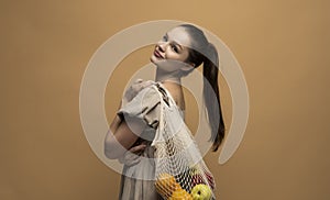 Young brunette woman with cotton reusable mesh bag full of fruits. Shopping without plastic packaging in plastic free