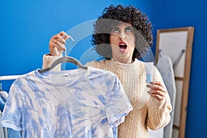 Young brunette woman with curly hair dyeing tye die t shirt angry and mad screaming frustrated and furious, shouting with anger