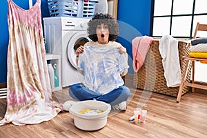 Young brunette woman with curly hair dyeing tye die t shirt and dress afraid and shocked with surprise and amazed expression, fear