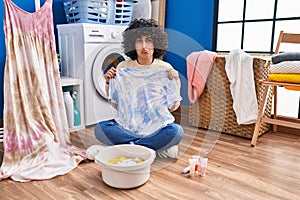 Young brunette woman with curly hair dyeing tye die t shirt and dress depressed and worry for distress, crying angry and afraid