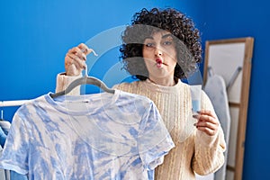 Young brunette woman with curly hair dyeing tye die t shirt making fish face with mouth and squinting eyes, crazy and comical
