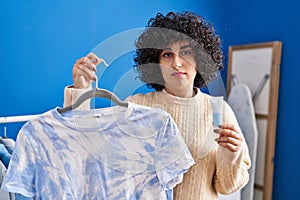 Young brunette woman with curly hair dyeing tye die t shirt relaxed with serious expression on face