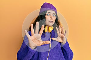 Young brunette woman with curly hair listening to music using headphones afraid and terrified with fear expression stop gesture