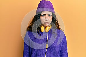 Young brunette woman with curly hair listening to music using headphones depressed and worry for distress, crying angry and afraid