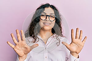 Young brunette woman with curly hair wearing casual clothes and glasses showing and pointing up with fingers number ten while