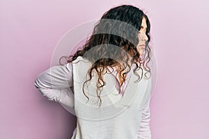 Young brunette woman with curly hair wearing casual clothes suffering of backache, touching back with hand, muscular pain