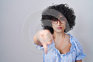 Young brunette woman with curly hair wearing glasses over isolated background looking unhappy and angry showing rejection and
