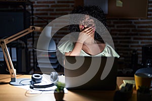 Young brunette woman with curly hair working at the office at night bored yawning tired covering mouth with hand