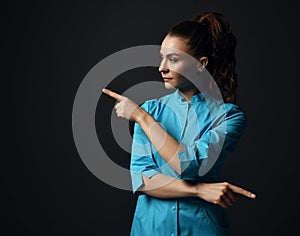 Young brunette woman doctor nurse in blue medical gown points with fingers in different directions diagonal