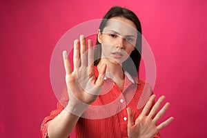 Young brunette woman does stop sign with palm against pink background