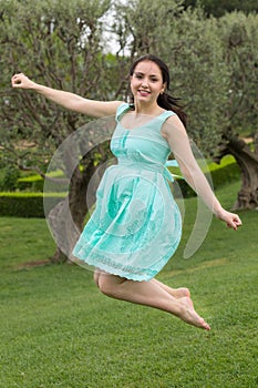 young brunette woman in dress jumping at the outdoors