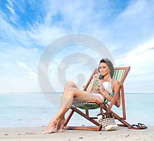 A young brunette woman drinking a cocktail and relaxing on the beach