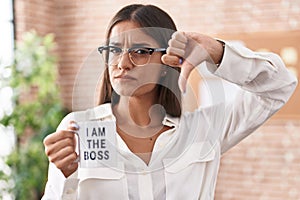 Young brunette woman drinking from i am the boss coffee cup with angry face, negative sign showing dislike with thumbs down,
