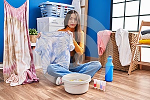 Young brunette woman dyeing tye die t shirt and dress skeptic and nervous, frowning upset because of problem