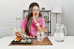 Young brunette woman eating sushi using chopsticks hand on mouth telling secret rumor, whispering malicious talk conversation