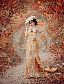 A young brunette woman with an elegant, hairstyle in a hat with a strass feathers. Lady in a yellow vintage dress walks