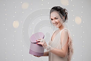 Young brunette woman in evening dress on a white background. Holding Christmas present box. Joy, happiness and surprise.