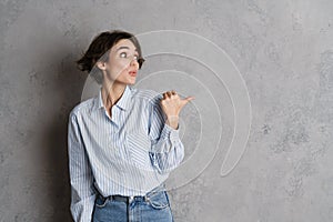 Young brunette woman expressing surprise and pointing finger aside