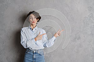 Young brunette woman expressing surprise and pointing fingers aside