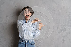 Young brunette woman expressing surprise and pointing fingers aside