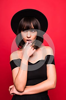 Young brunette woman in fluppy hat and black clothes on red background