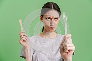 Young brunette woman frown while showing disposable forks