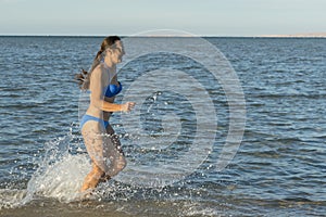 A young brunette woman or girl wearing a bikini running through the surf on a deserted tropical beach with a blue sky. Young