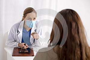 Young brunette woman having consultation at doctor office during coronavirus and flu outbreak. Female doctor wearing