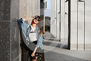 A young brunette woman in hipster clothes and round eyeglasses posing outdoors on a summer day