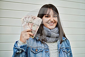 Young brunette woman holding arabia saudi riyal banknotes by shutter door photo