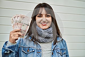 Young brunette woman holding arabia saudi riyal banknotes by shutter door photo