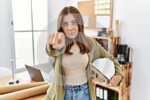 Young brunette woman holding architect hardhat at the office pointing with finger to the camera and to you, confident gesture