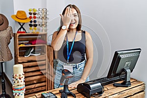 Young brunette woman holding banner with open text at retail shop covering one eye with hand, confident smile on face and surprise