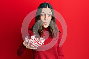 Young brunette woman holding bowl full of pills scared and amazed with open mouth for surprise, disbelief face