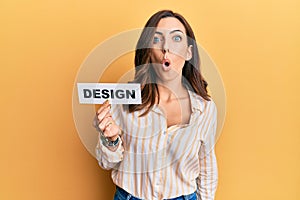 Young brunette woman holding design paper scared and amazed with open mouth for surprise, disbelief face